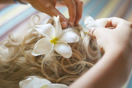 Beautiful, cute blond bride doing hair with flowers before wedding day. Long lashes, white flowers, smilling and happy.の写真素材