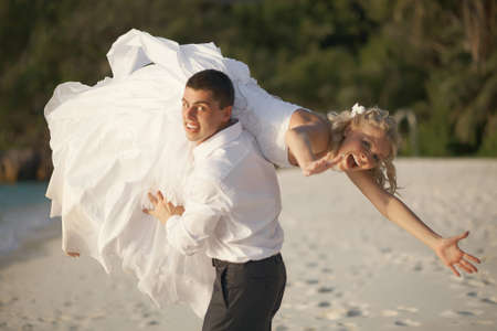 Beautiful young couple enjoying sunset, walking barefoot on beach and playing with each other. Lifestyle weding on tropical island in caribbean or Hawaii.の写真素材