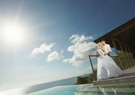 Beautiful young couple standing close to pool before wedding. Warm summer day, clear sky and water, wedding preparations at tropical caribbean island or Hawaii.の写真素材
