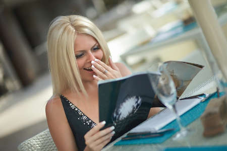 Lovely, attractive woman sitting in restaurant and reading magazine. Warm summer day, lovely outfit and beautiful haircut.の写真素材