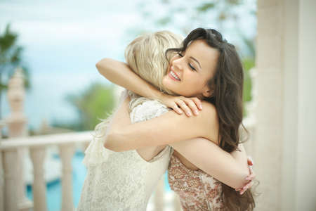 Gorgeous, lovely bride hugging, embracing beautiful best friend before wedding day. Lifestyle happiness during wedding day.の写真素材