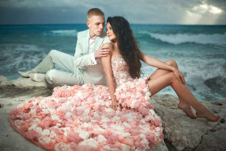 Beautiful, charming and sexy couple kissing on rocks, cliffs during sunset. Windy day at paradise.の写真素材