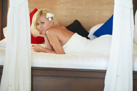 Gorgerous bride lying and relaxing on bed before exotic wedding ceremony on island. Canopy bed in spacious bedroom.の写真素材