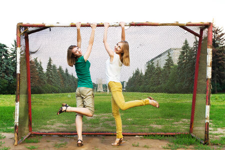 Young women having fun hanging by vintage soccer goal. Attractive girls having fun on a soccer field