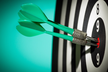  Darts arrows in the target center against a green background. Darts hitting a target close-up.の写真素材