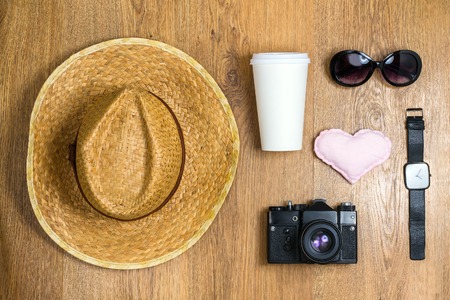 Top view of braided hat, pair of glasses, vintage camera, takeaway cup, watch and cute cloth heart on a wooden background. Travel conceptの写真素材
