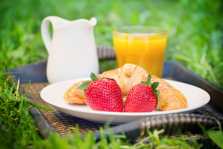 Breakfast outdoors with croissant and strawberries, orange juice and milk jugの写真素材
