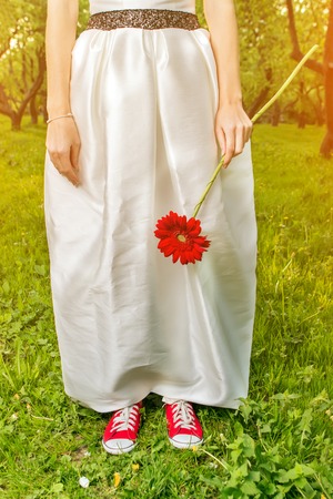 Bride in sneakers holding a flower in summer parkの写真素材