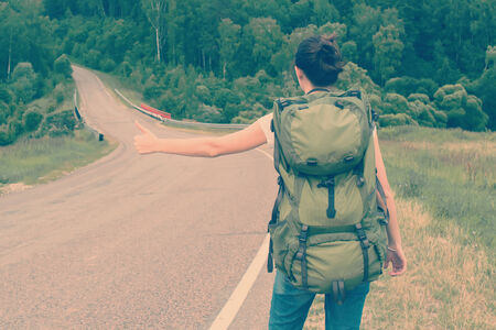 Woman with backpack hitchhiking on a road. Toned imageの写真素材