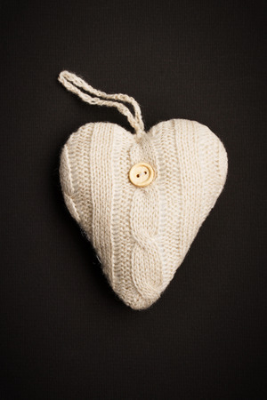 Knitted heart with sewing button on it against black backgroundの写真素材