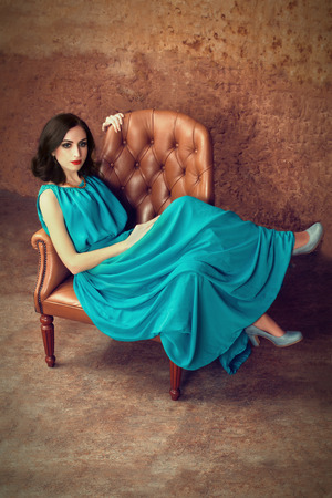 Attractive woman in elegant blue dress relaxing in leather armchairの写真素材