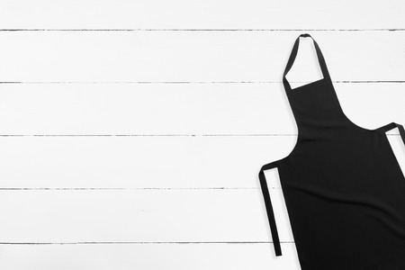 Blank black apron on white wooden background with copy spaceの写真素材