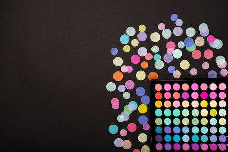 Make-up eyeshadow palette with confetti scattered on black background. Free space for your promo copyの写真素材