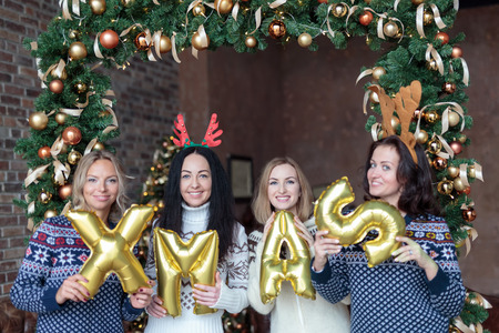 Young women holding word xmas made of golden balloons with Christmas fir tree decoration on backgroundの写真素材