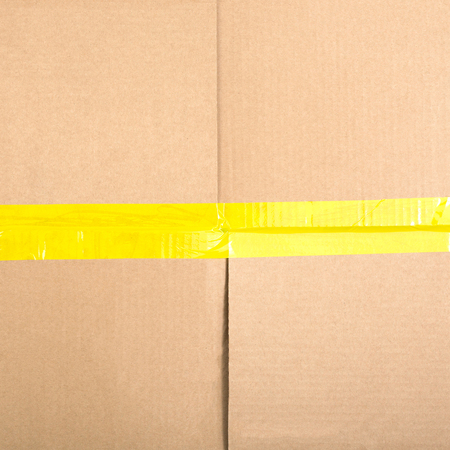 Square cardboard box with a sticky tape. Cardboard background. Top viewの写真素材