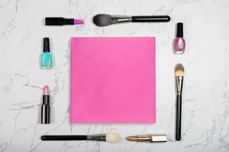 Flat lay of cosmetic products with blank pink paper card on white marble background. Makeup mockup. Lipstick, brushes and nail polish on marble texureの写真素材