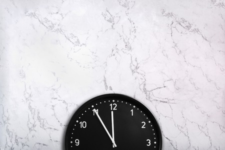 Black wall clock on white marble texture. Office clock on marble background
