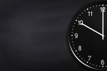 Closeup of black wall clock on black chalkboard texture. Crop image with copyspaceの写真素材