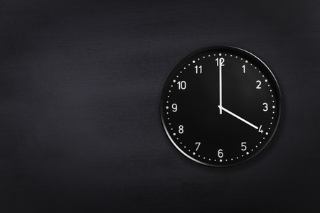 Black wall clock showing four o'clock on black chalkboard background. Office clock showing 4am or 4pm on black textureの写真素材