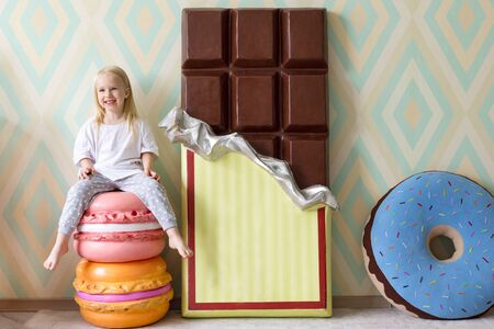 Cute little child sitting with a chocolate bar, macaroons and donut toysの写真素材