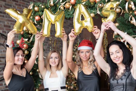 Young happy women wearing dresses showing golden helium balloons forming word xmas.の写真素材