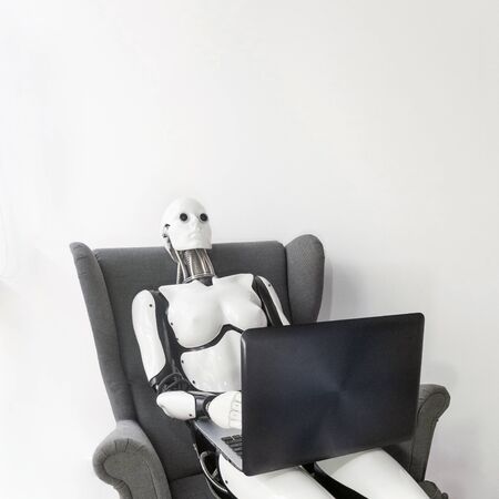 Robot working with laptop while sitting in armchair against white wall