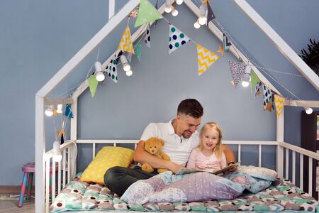 Father dad in bed with daughter reading stories at bedtime. Closeness relationship and loveの写真素材