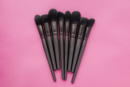 Flat lay of black makeup brushes collection on pink background. Cosmetic make-up brushes set.