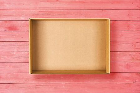 Open cardboard box on pink background. Empty cardboard package on pink wooden texture. Flat layの写真素材