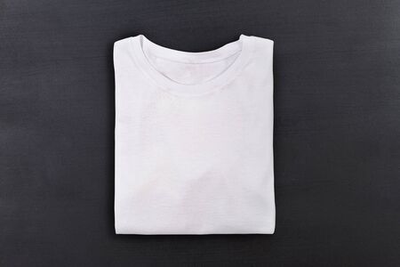 White folded t-shirt on black chalkboard background. Flat lay. Top view