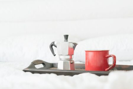 Coffee mug with steel coffee percolator on wooden tray on bed