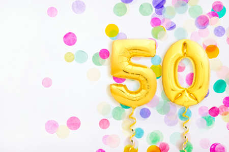 Number 50 fifty made of golden inflatable balloons with golden ribbons on colorful confetti...