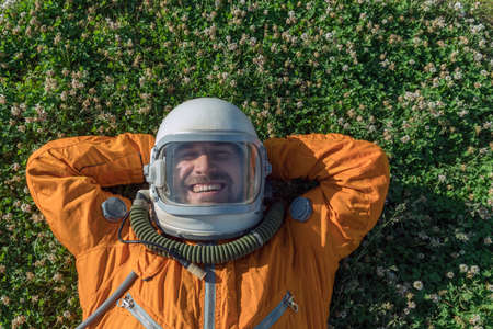 Closeup of cosmonaut wearing space suit and helmet having a rest while lying on green grass outdoor. Top viewの写真素材