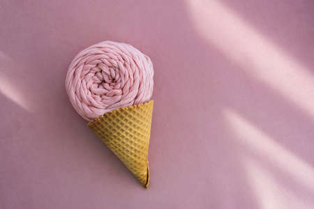 Top view of pink macrame yarn skein in ice cream waffle cone on a pink background with sunlight...