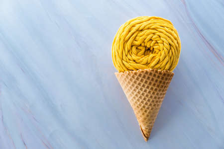 Flat lay of yellow macrame yarn skein in ice cream waffle cone on a marble background