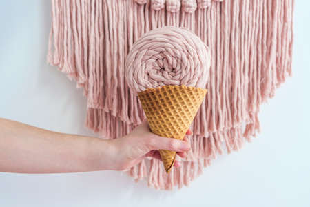 Pink macrame yarn skein in ice cream cone in woman hand.