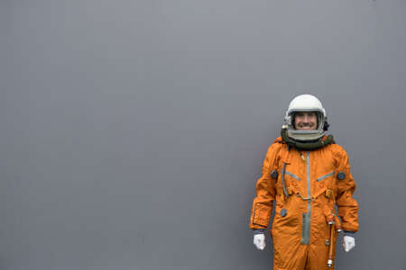 Astronaut wearing orange space suit and helmet standing against gray wall backgroundの写真素材