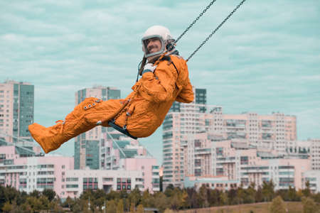 Happy astronaut smiling and looking at camera while swinging on swing outdoors.の写真素材