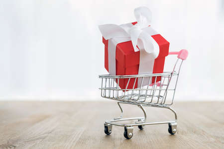 Closeup of miniature shopping cart with red gift box with a bow on a wooden tableの写真素材