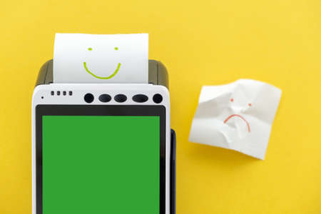 POS terminal with touchscreen green display with printed reciept with a smile picture on a yellow backgroundの写真素材