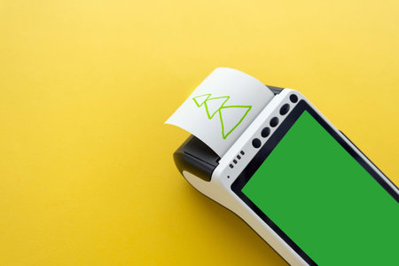 Credit card POS terminal with touchscreen green display with printed reciept with a Christmas tree picture on a yellow background with a space for your copyの写真素材