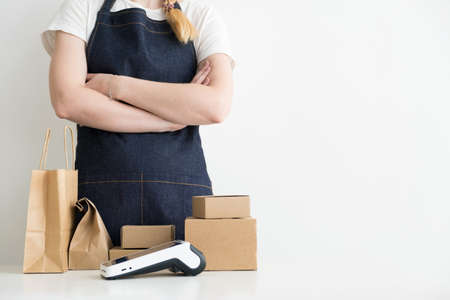 Business woman with the arms crossed standing by the table with carton boxes, cardboard packages and modern payment POS terminalの写真素材