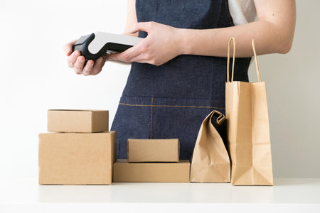 Closeup of busines woman holding modern payment POS terminal with carton boxes, cardboard packages and kraft bags on the tableの写真素材