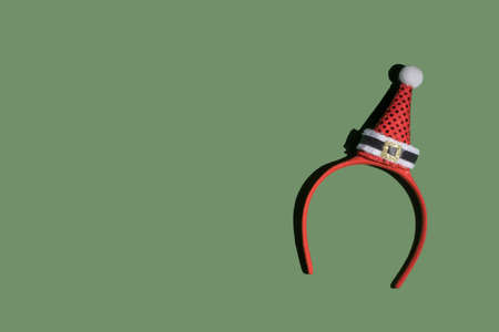 Red Christmas headband with cute red Santa hat on green background. Flat lay.の写真素材