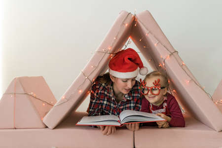 Mother with daughter wearing pajamas and Christmas hat and headband reading a book in a baby room....