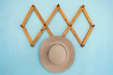Wooden hanger with beige suede hat on blue wall. Wooden hook for clothes on blue backgroundの写真素材