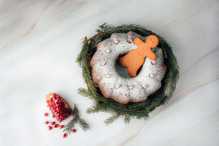 Gingerbread men nestled in holiday cake with pomegranate on marble table background. Christmas cake with icing and festive decoration.の写真素材