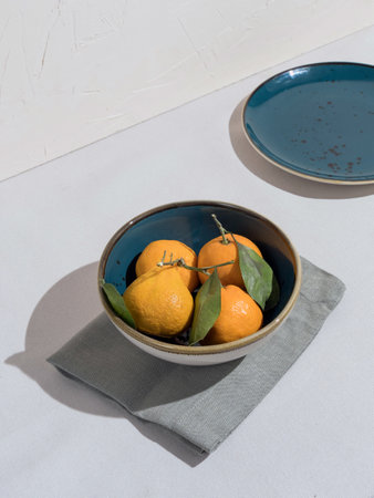 Blue bowl of orange tangerines on table with tableclothの写真素材