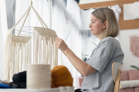 Woman making macrame lampshade using white cord to tie the strings together. Woman knits lampshade...