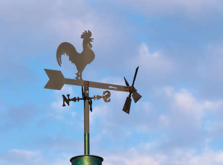 metal wind vane with rooster silhouette on defocused background of clouds